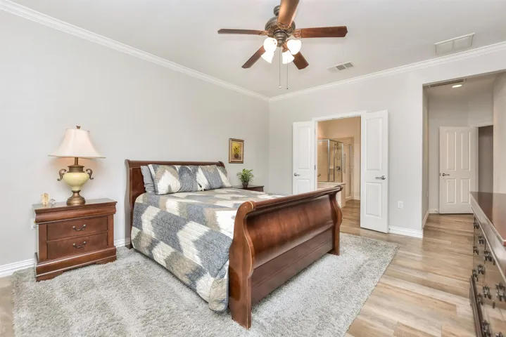 Bedroom with crown molding, a ceiling fan, baseboards, visible vents, and light wood-style floors