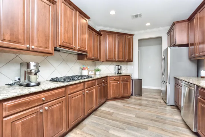 Kitchen with backsplash, light stone countertops, appliances with stainless steel finishes, visible vents, and light wood-style floors