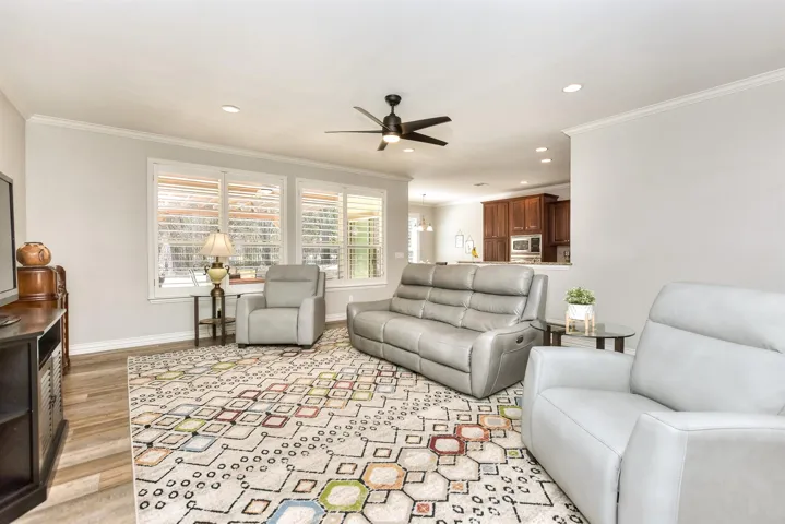 Living area with light wood-type flooring, baseboards, crown molding, and a ceiling fan