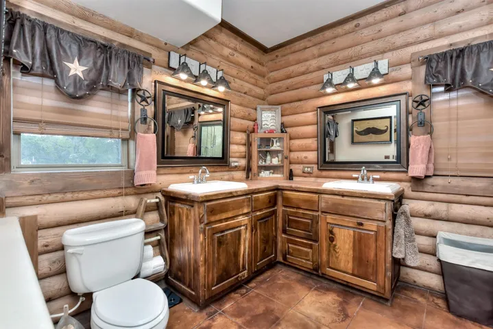 Bathroom with toilet, log walls, and a sink