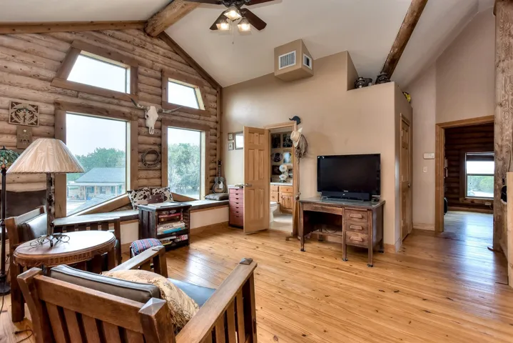Living room with high vaulted ceiling, light wood-style floors, beamed ceiling, visible vents, and a ceiling fan
