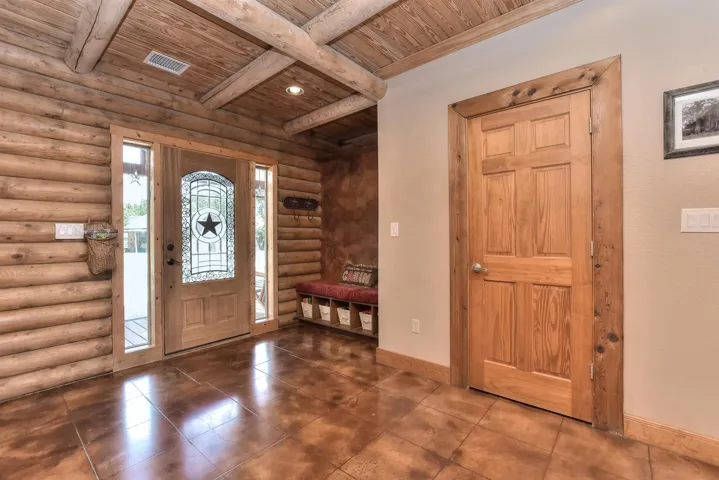 Entrance foyer featuring wooden ceiling, rustic walls, tile patterned flooring, baseboards, and beamed ceiling