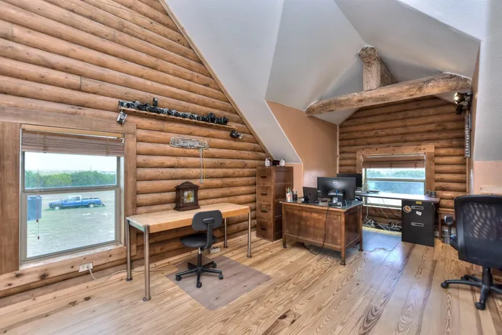 Office with log walls, light wood-style floors, and vaulted ceiling