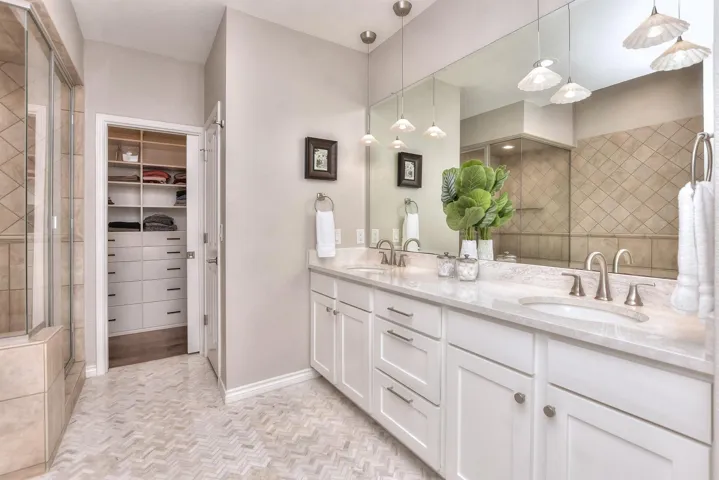 Bathroom with tiled shower, double vanity, a spacious closet, and dual vanity/sinks