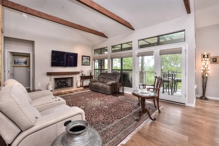 Living room featuring wood finished floors, beamed ceiling, high ceiling, and a fireplace with raised hearth