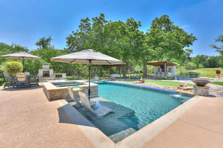 View of swimming pool featuring an outdoor stone fireplace, a patio area, a pool with connected hot tub, and an outdoor structure