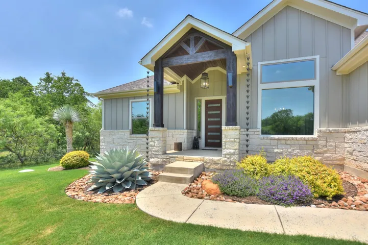 View of front of home featuring board and batten siding, stone siding, a front yard, and a shingled roof
