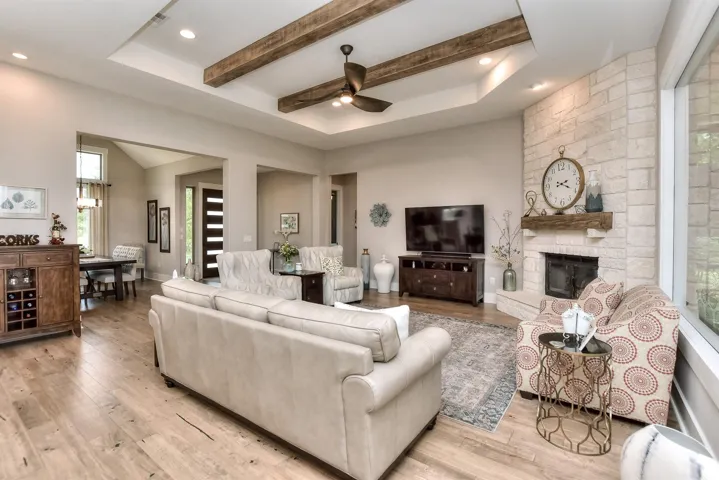 Living area with light wood-style flooring, ceiling fan, a raised ceiling, a fireplace, and beam ceiling