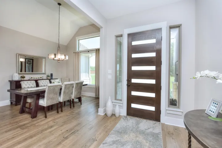 Entryway with a chandelier, light wood finished floors, vaulted ceiling, and baseboards