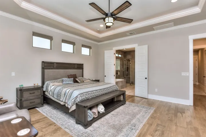 Bedroom featuring a raised ceiling, ornamental molding, light wood-type flooring, recessed lighting, and connected bathroom