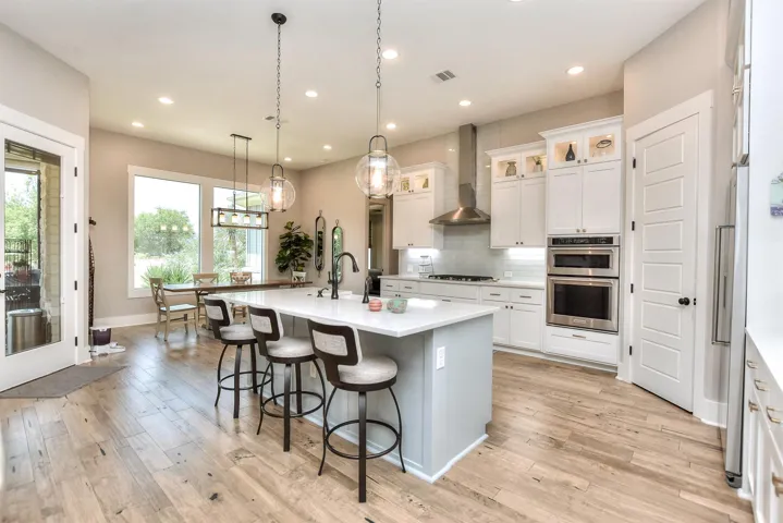 Kitchen with wall chimney exhaust hood, stainless steel appliances, a kitchen island with sink, a breakfast bar, and recessed lighting