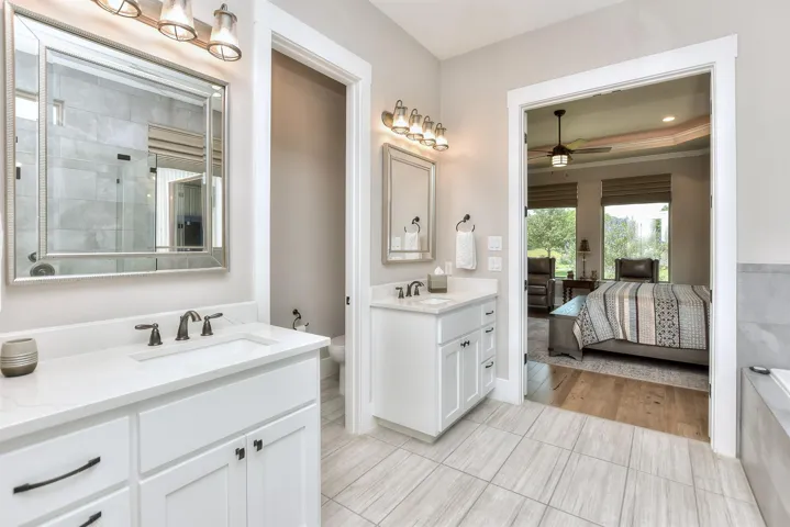 Ensuite bathroom featuring ceiling fan, two vanities, toilet, and tile patterned floors