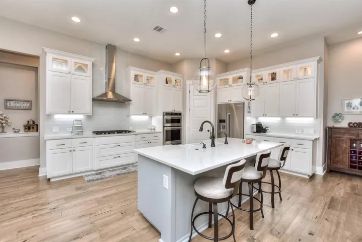 Kitchen featuring stainless steel appliances, a sink, wall chimney range hood, a center island with sink, and tasteful backsplash
