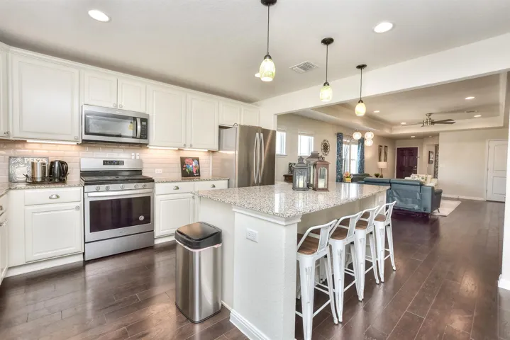Kitchen with stainless steel appliances, dark wood finished floors, white cabinetry, a center island, and light stone counters