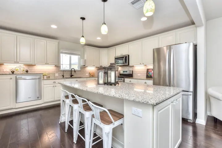 Kitchen with appliances with stainless steel finishes, a sink, a kitchen island, white cabinetry, and decorative backsplash