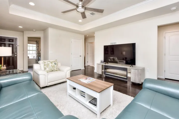 Living area featuring a ceiling fan, ornamental molding, recessed lighting, a tray ceiling, and wood finished floors