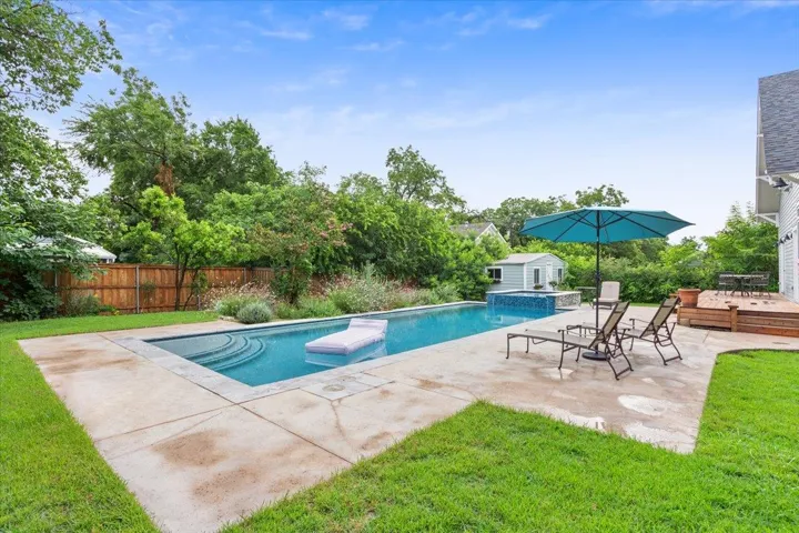 View of swimming pool featuring a fenced backyard, a deck, a storage unit, a pool with connected hot tub, and a patio area