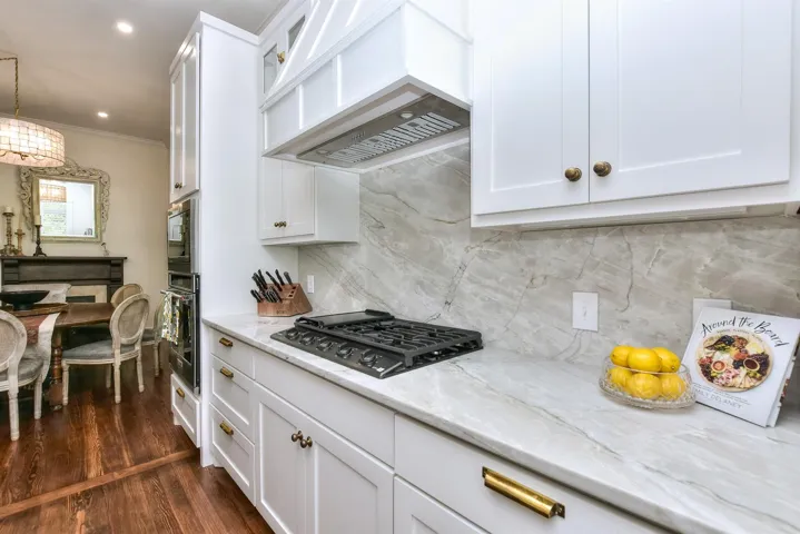Kitchen with custom range hood, black cooktop, stainless steel oven, crown molding, and light stone countertops