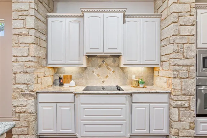 Kitchen with light stone counters, decorative backsplash, white cabinetry, and stainless steel appliances