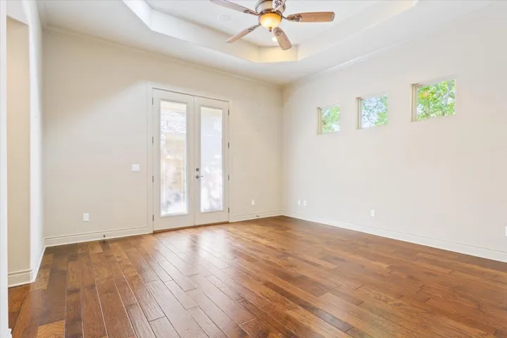 Empty room featuring a raised ceiling, french doors, hardwood / wood-style floors, ceiling fan, and ornamental molding