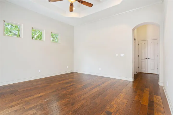 Unfurnished room featuring dark wood-style flooring, a tray ceiling, arched walkways, a ceiling fan, and ornamental molding