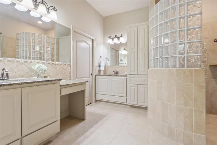 Full bath featuring a walk in shower, light tile patterned floors, two vanities, tasteful backsplash, and tile walls