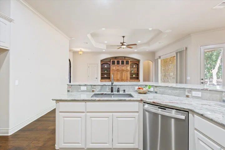 Kitchen featuring white cabinetry, dishwasher, light stone countertops, dark wood-style floors, and crown molding