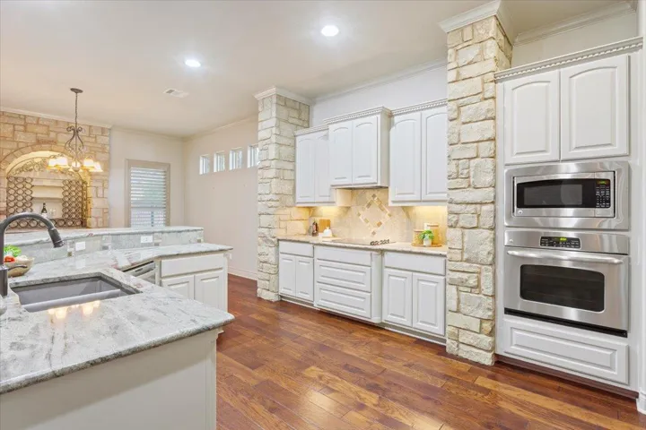 Kitchen featuring ornamental molding, appliances with stainless steel finishes, dark wood-style floors, light stone countertops, and decorative light fixtures