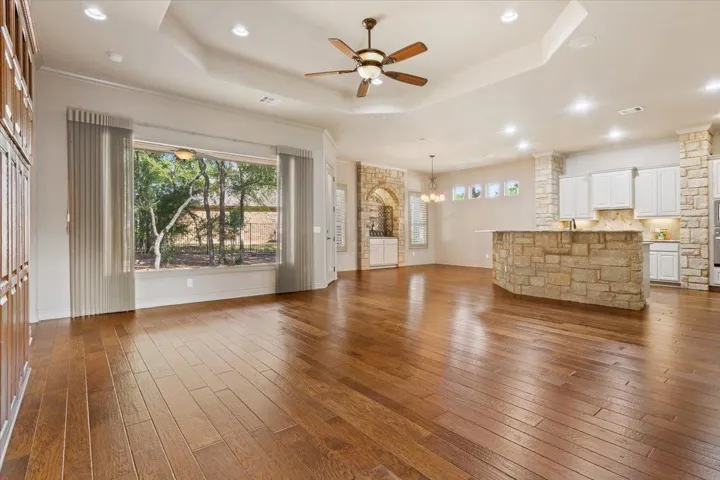 Unfurnished living room with a tray ceiling, dark wood-style flooring, a ceiling fan, recessed lighting, and a chandelier