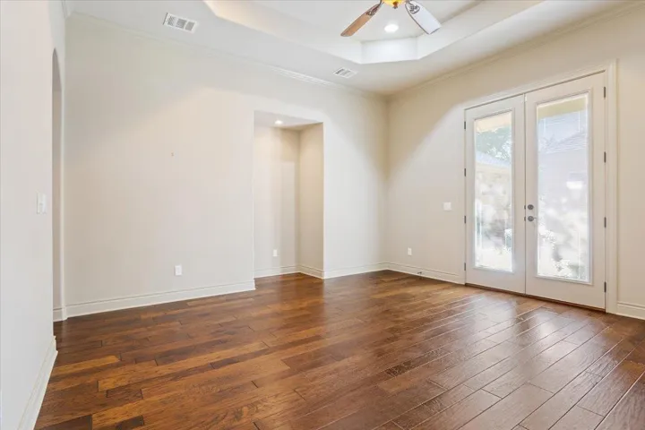 Spare room featuring a raised ceiling, crown molding, french doors, ceiling fan, and dark wood-style floors