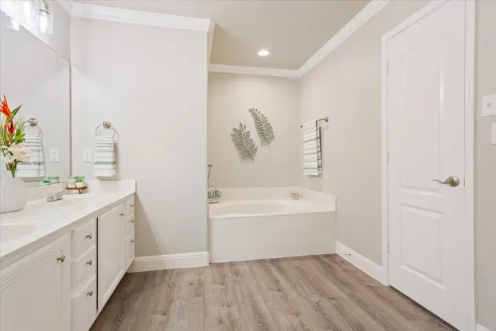 Full bathroom with a garden tub, double vanity, light wood finished floors, crown molding, and recessed lighting