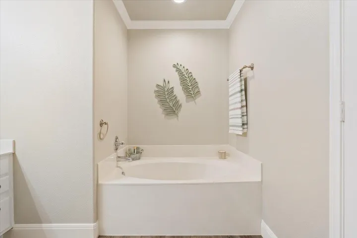 Bathroom featuring a bath, vanity, ornamental molding, and a textured wall