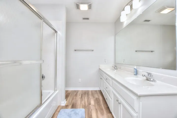 Full bath featuring double vanity, light wood-style flooring, and bath / shower combo with glass door