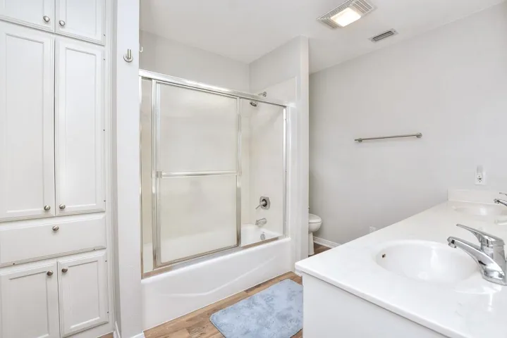 Full bath featuring shower / bath combination with glass door, double vanity, and light wood-type flooring