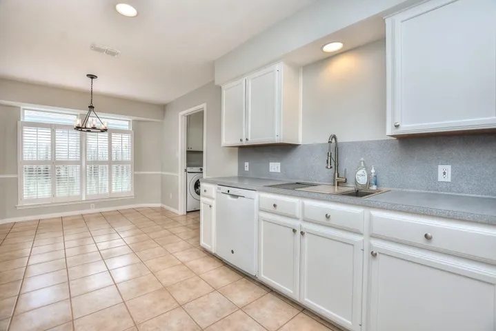 Kitchen with light countertops, white cabinetry, dishwasher, washer / dryer, and pendant lighting