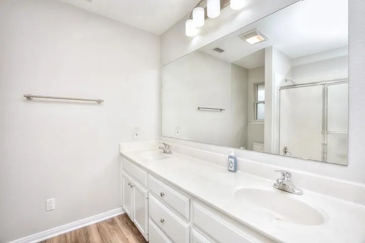 Full bath featuring double vanity, a stall shower, and light wood-style flooring