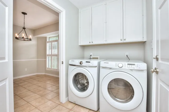 Laundry room featuring light tile patterned floors, washer and dryer, a chandelier, and cabinet space