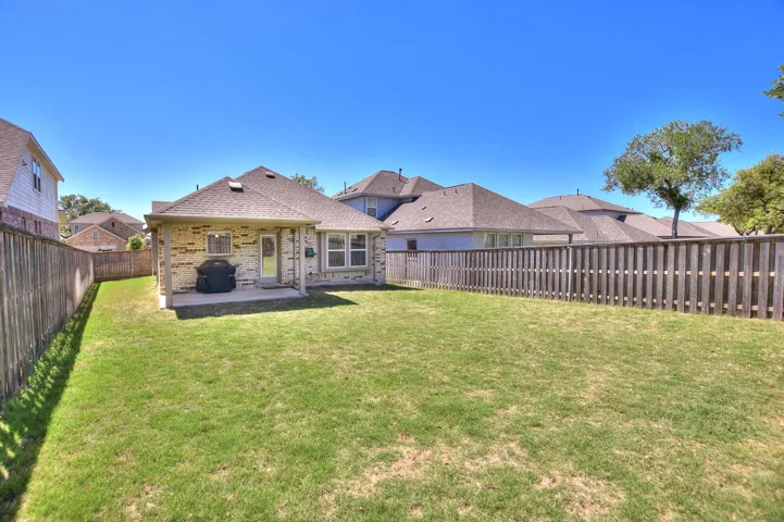 Back of property with a shingled roof, a patio area, a lawn, a fenced backyard, and brick siding