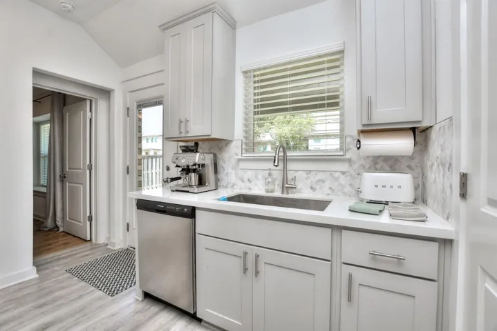 Kitchen with tasteful backsplash, light countertops, light wood-style floors, stainless steel dishwasher, and a sink
