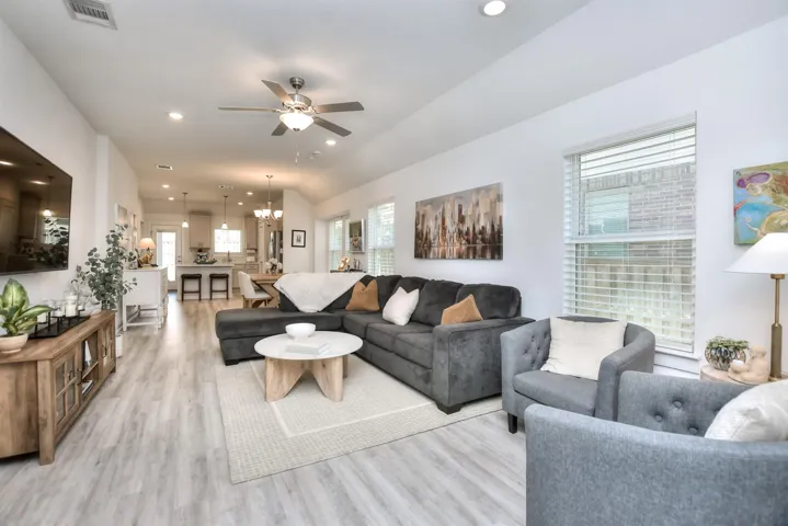 Living room with visible vents, recessed lighting, vaulted ceiling, ceiling fan with notable chandelier, and light wood-style flooring