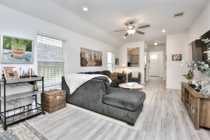 Living room with visible vents, baseboards, a ceiling fan, light wood-style floors, and vaulted ceiling