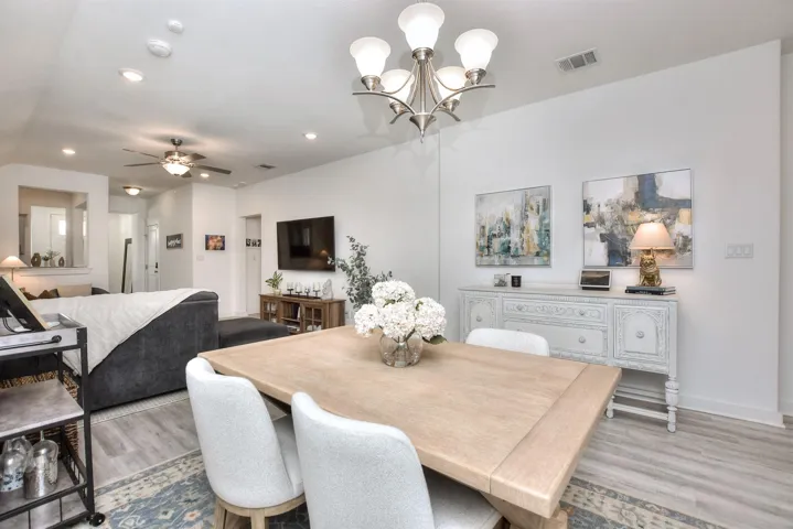 Dining area featuring light wood-type flooring, baseboards, recessed lighting, visible vents, and ceiling fan with notable chandelier