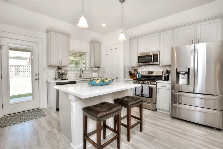 Kitchen with tasteful backsplash, light countertops, light wood-type flooring, appliances with stainless steel finishes, and a breakfast bar area