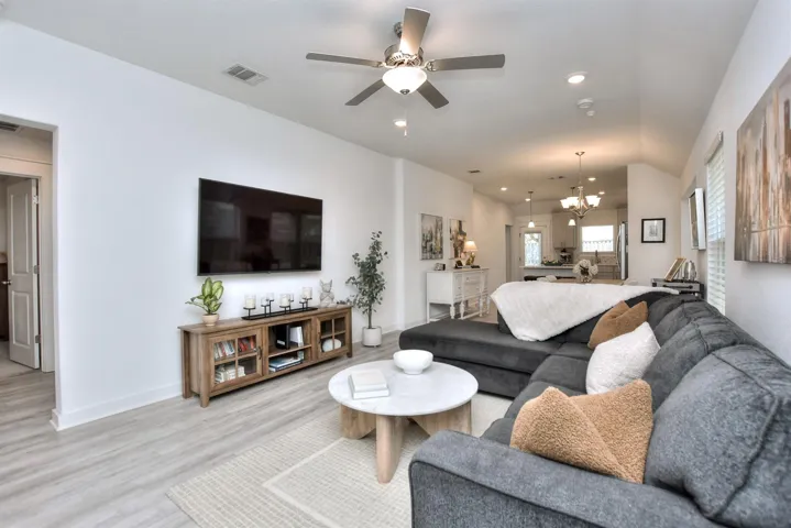 Living room with ceiling fan with notable chandelier, light wood-type flooring, visible vents, recessed lighting, and baseboards