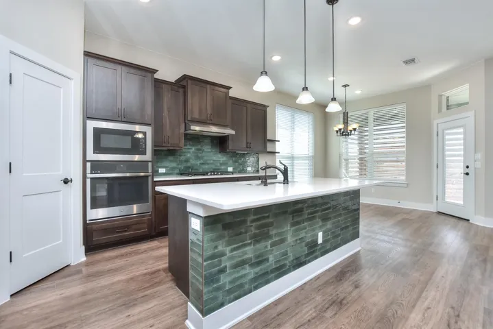 Kitchen with dark wood finish cabinetry, stainless steel appliances, a center island with sink, tasteful backsplash