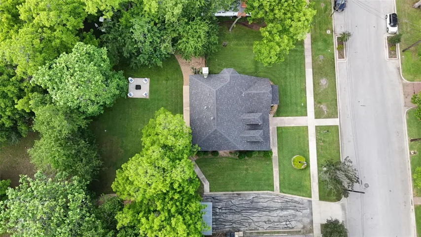 Aerial perspective showcasing a pitched roof with multiple dormers, extensive mature tree coverage, and a spacious front lawn with concrete walkways