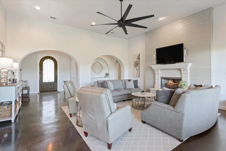 Living room featuring ceiling fan, arched walkways, a glass covered fireplace with Wooden wall behind it reaching to the ceiling,  recessed lighting, and Stained & finished concrete floors