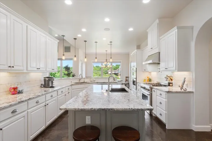 Kitchen featuring breakfast bar for two on this end of the kitchen, high end range, extractor fan, recessed lighting, and white cabinet...s