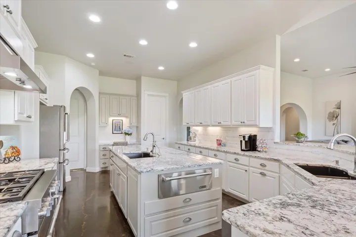 Kitchen with a  double sink for doing dishes plus a sink in the center island.  The center island also features a warming drawer,  cabinets & drawers & a small breakfast bar for 2.  Tasteful recessed lighting, &  upgraded granite countertops...