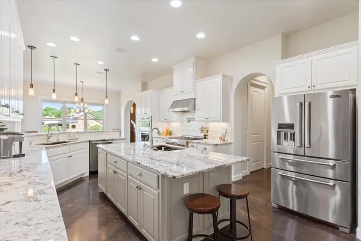 Kitchen featuring stainless steel appliances, arched, entries, stainless exhaust hood, and natural stone backsplash.  All appliances are stainless & are Jenn-Air brand!